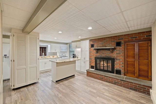 kitchen featuring white cabinetry, a center island, light stone countertops, light hardwood / wood-style flooring, and white appliances