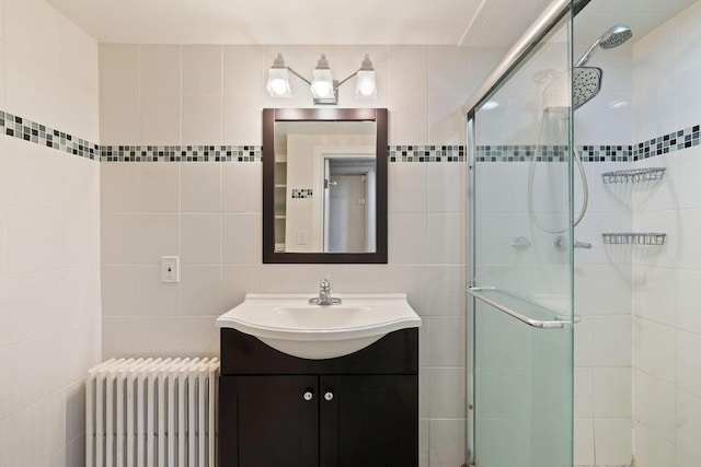 bathroom featuring radiator heating unit, vanity, tile walls, and a shower with shower door