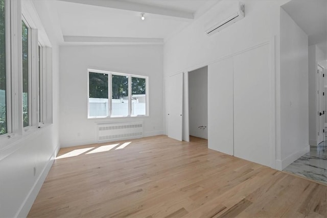 empty room with radiator heating unit, lofted ceiling with beams, light hardwood / wood-style floors, and a wall mounted AC