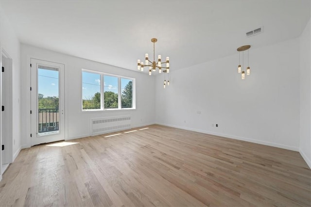 spare room featuring radiator heating unit, light hardwood / wood-style flooring, and a notable chandelier