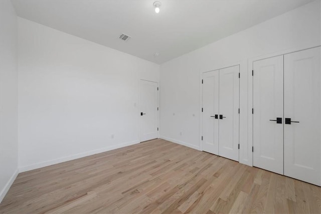 unfurnished bedroom with two closets and light hardwood / wood-style floors