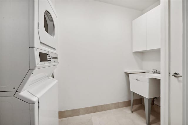 clothes washing area with stacked washer / drying machine, light tile patterned floors, and cabinets