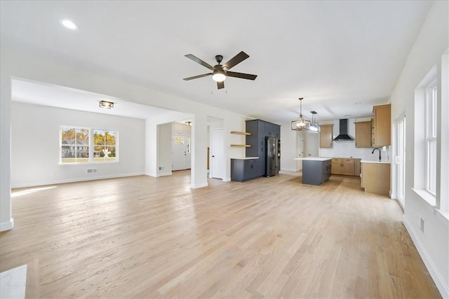 unfurnished living room with ceiling fan with notable chandelier, light hardwood / wood-style floors, and sink