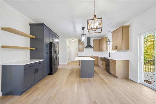 kitchen with stainless steel appliances, wall chimney range hood, decorative light fixtures, a center island, and light hardwood / wood-style floors