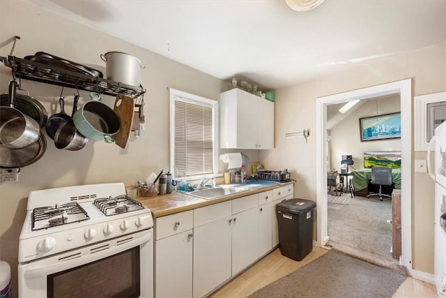 kitchen featuring white gas range oven, vaulted ceiling, sink, light hardwood / wood-style flooring, and white cabinets