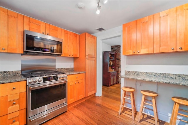 kitchen featuring light hardwood / wood-style floors, light stone counters, a breakfast bar area, and appliances with stainless steel finishes