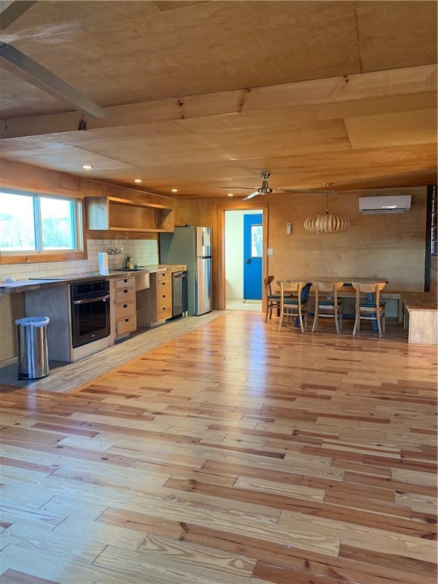 kitchen with appliances with stainless steel finishes, ceiling fan, decorative light fixtures, an AC wall unit, and light hardwood / wood-style floors