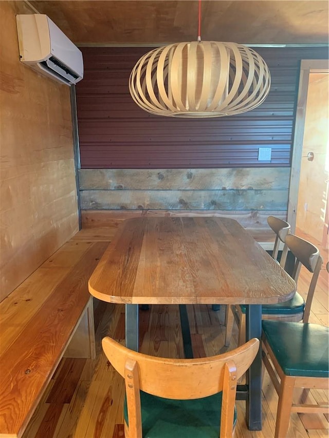 dining space with light wood-type flooring, a wall mounted AC, and wooden walls