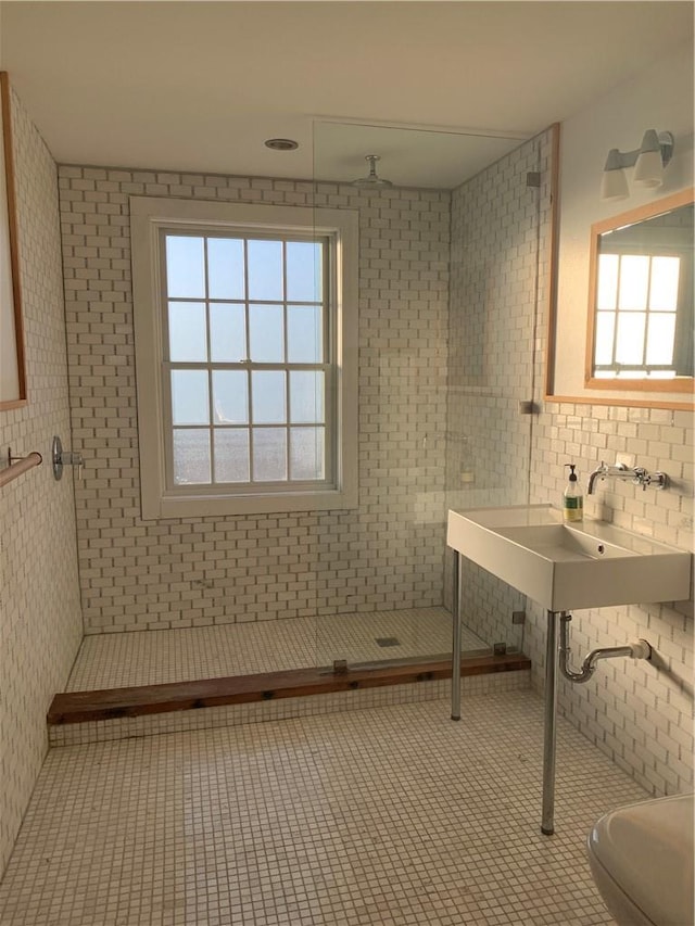 bathroom featuring a tile shower, tile patterned flooring, a healthy amount of sunlight, and tile walls