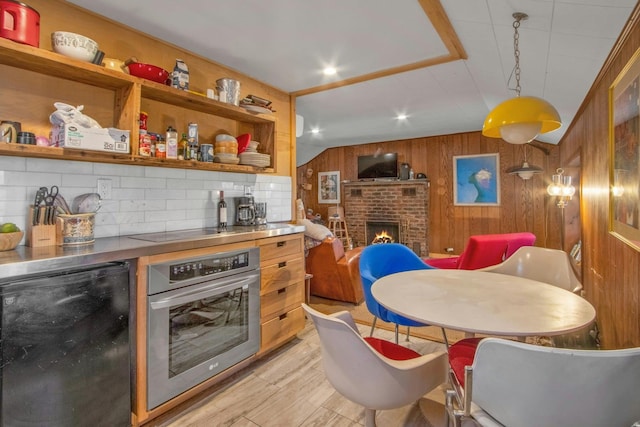 kitchen featuring hanging light fixtures, wooden walls, a fireplace, black appliances, and light wood-type flooring