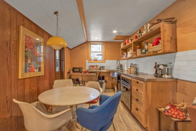 dining room featuring vaulted ceiling, sink, wooden walls, and light hardwood / wood-style flooring