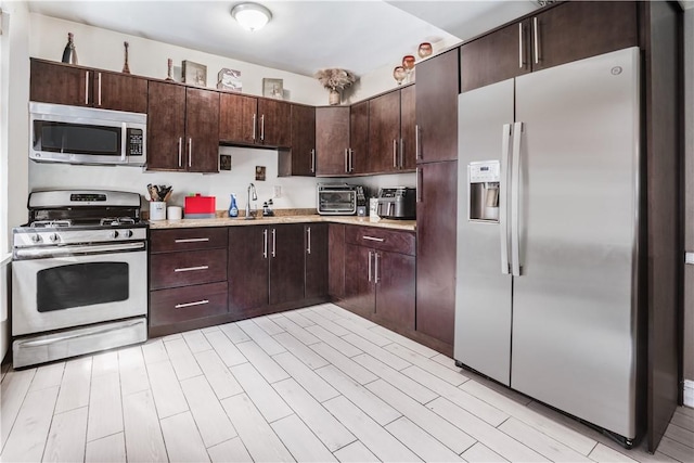 kitchen with dark brown cabinetry, stainless steel appliances, light hardwood / wood-style flooring, and sink