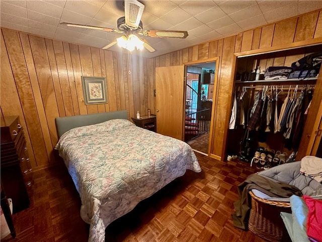 bedroom with dark parquet floors, wood walls, ceiling fan, and a closet