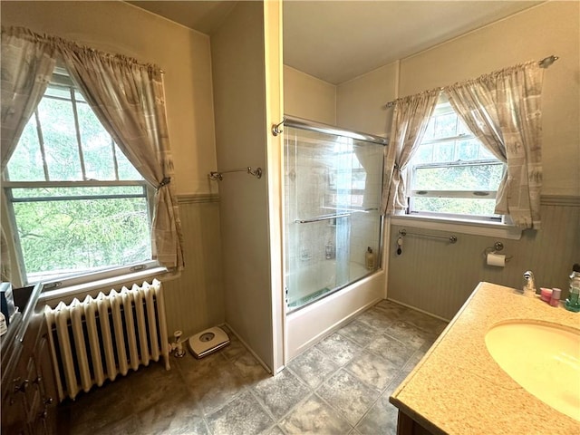 bathroom featuring radiator heating unit, vanity, and bath / shower combo with glass door