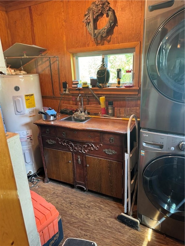 clothes washing area with electric water heater, sink, wood-type flooring, stacked washer and dryer, and wood walls