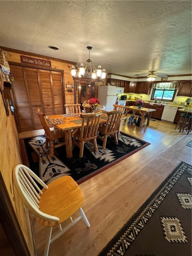 dining space featuring a textured ceiling, wooden walls, ceiling fan with notable chandelier, and light wood-type flooring