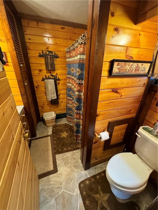 bathroom featuring toilet, a textured ceiling, and wooden walls