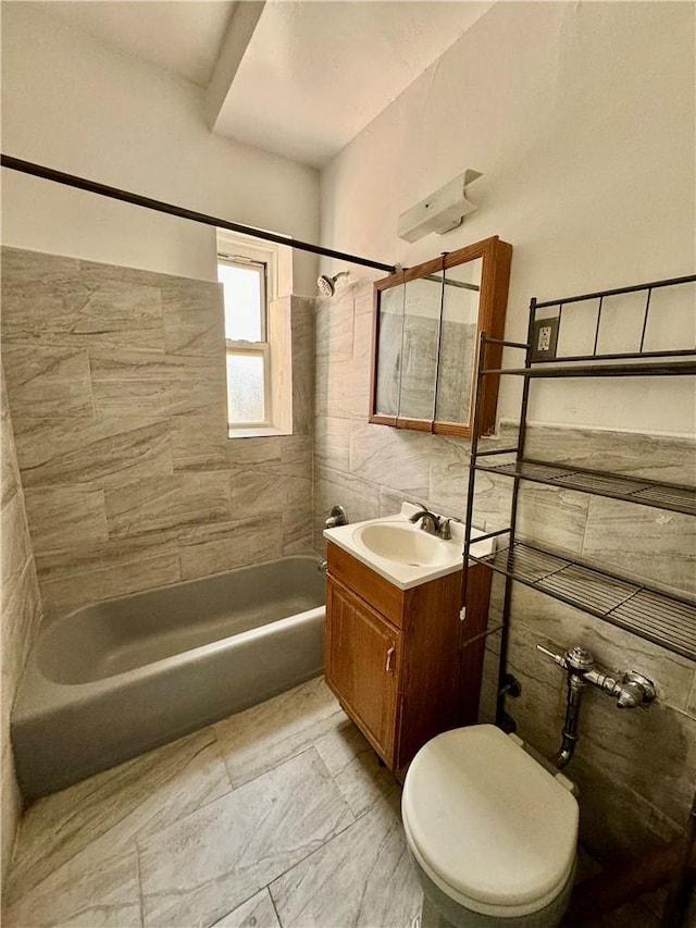 full bathroom featuring vanity, toilet, tiled shower / bath, and tile walls