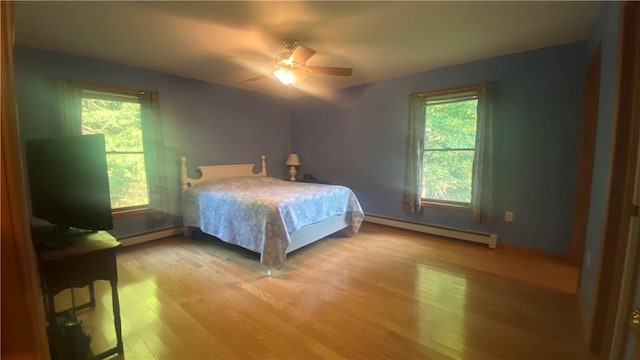 bedroom with ceiling fan, light hardwood / wood-style flooring, multiple windows, and a baseboard heating unit