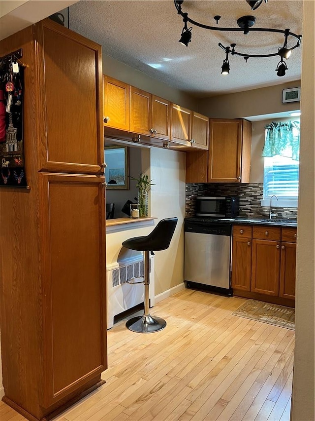 kitchen with tasteful backsplash, a textured ceiling, stainless steel appliances, sink, and light hardwood / wood-style flooring