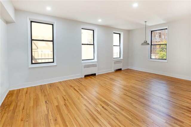 unfurnished room featuring radiator heating unit, light hardwood / wood-style floors, and a healthy amount of sunlight