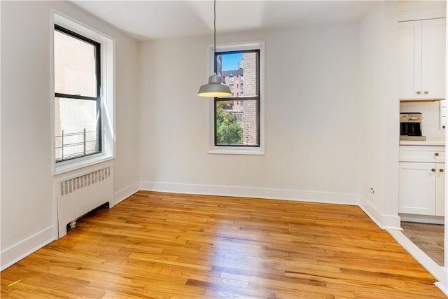unfurnished dining area featuring radiator heating unit, light wood-type flooring, and a healthy amount of sunlight