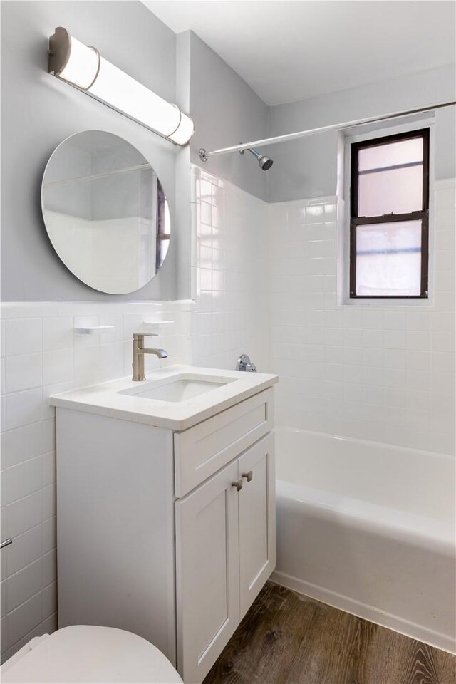 full bathroom with wood-type flooring, toilet, vanity, tile walls, and tiled shower / bath