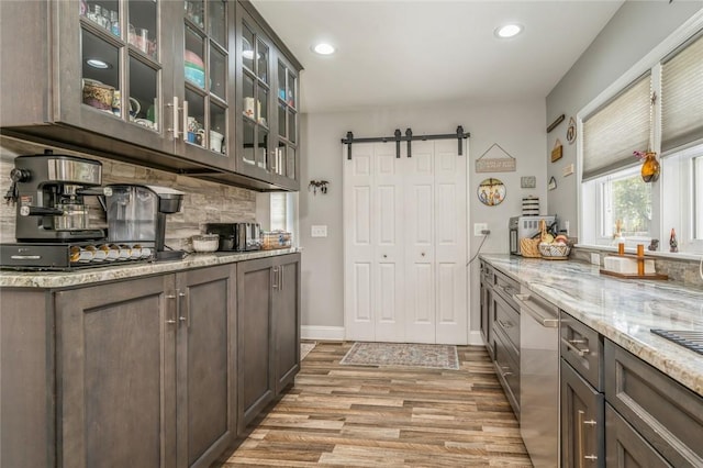 kitchen with a barn door, light stone countertops, light hardwood / wood-style flooring, and dark brown cabinets