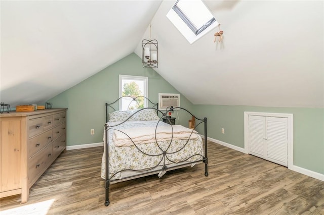 bedroom featuring hardwood / wood-style floors, a closet, lofted ceiling with skylight, and an AC wall unit