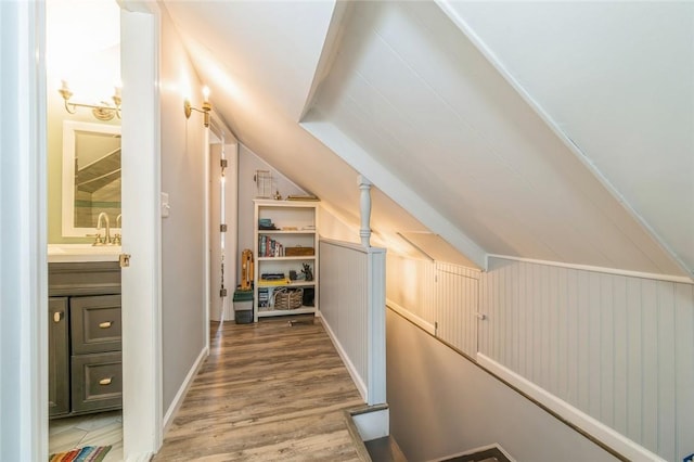 corridor featuring wood-type flooring, wood walls, lofted ceiling, and sink