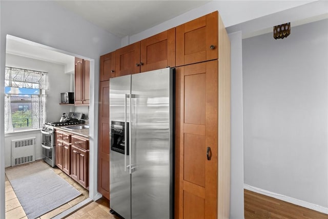 kitchen with light wood-type flooring, radiator heating unit, and stainless steel appliances