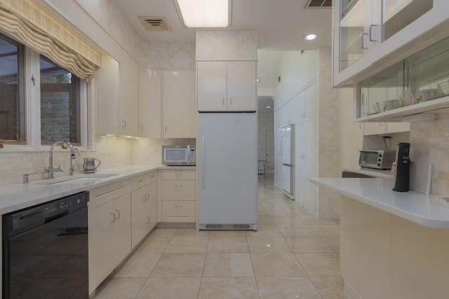 kitchen with white appliances, backsplash, sink, light tile patterned floors, and white cabinetry