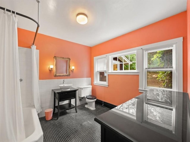 full bathroom featuring toilet, shower / bathtub combination with curtain, sink, and tile walls