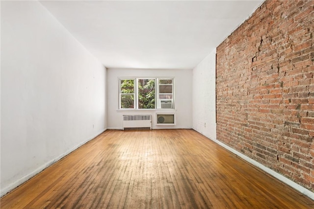 unfurnished living room with hardwood / wood-style floors, radiator heating unit, and brick wall