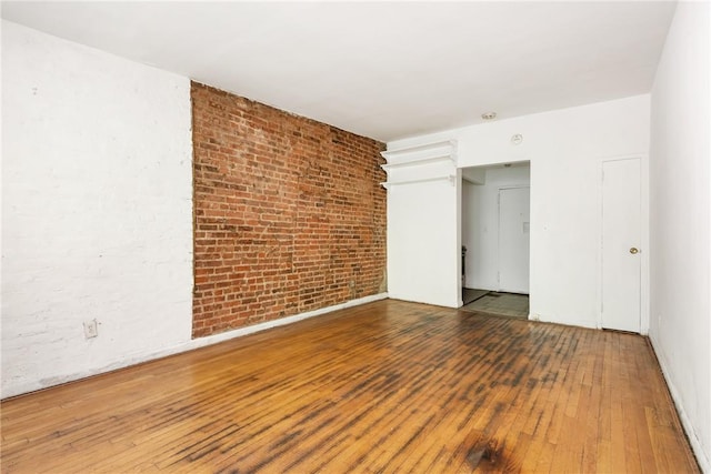 spare room with hardwood / wood-style flooring and brick wall