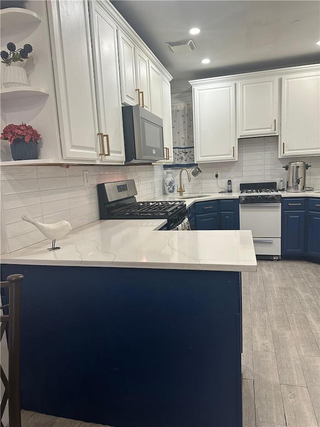 kitchen featuring appliances with stainless steel finishes, sink, blue cabinetry, white cabinets, and light hardwood / wood-style floors