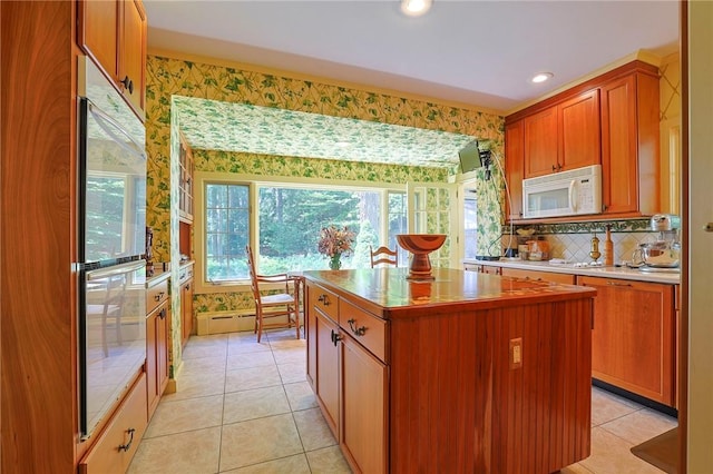 kitchen with light tile patterned floors, stainless steel double oven, a kitchen island, and backsplash