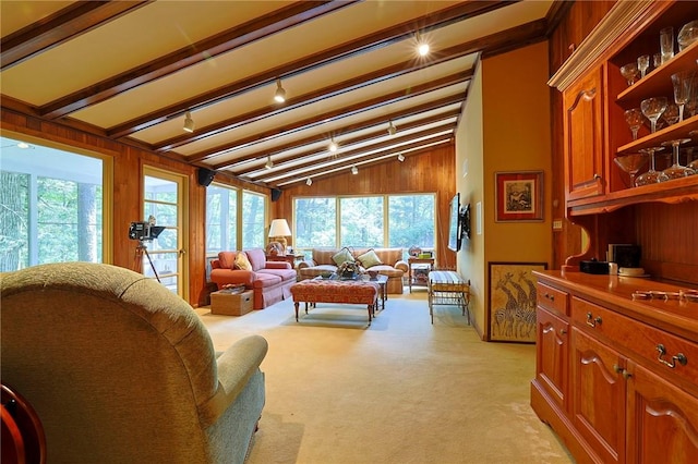 living room with vaulted ceiling with beams, wood walls, light colored carpet, and plenty of natural light