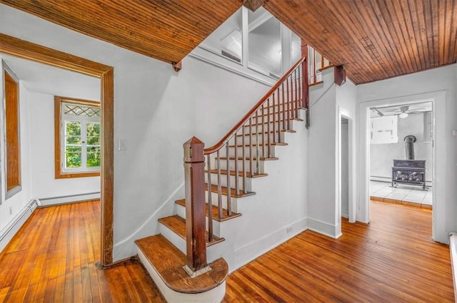 stairs featuring hardwood / wood-style floors, a wood stove, a baseboard heating unit, and wooden ceiling