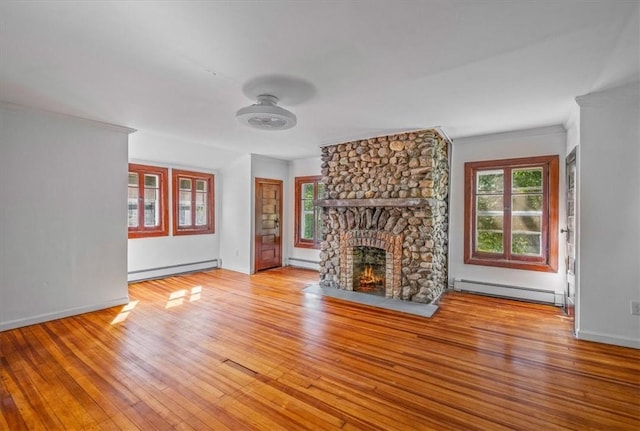 unfurnished living room with a stone fireplace, baseboard heating, and plenty of natural light