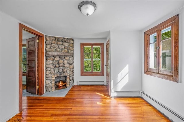 unfurnished living room featuring a stone fireplace, light hardwood / wood-style flooring, and a baseboard heating unit