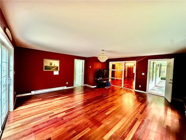 unfurnished living room with baseboard heating, a wealth of natural light, a chandelier, and wood-type flooring