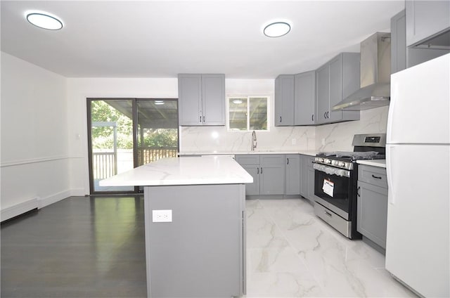 kitchen featuring gray cabinetry, a center island, wall chimney range hood, stainless steel gas range, and white fridge