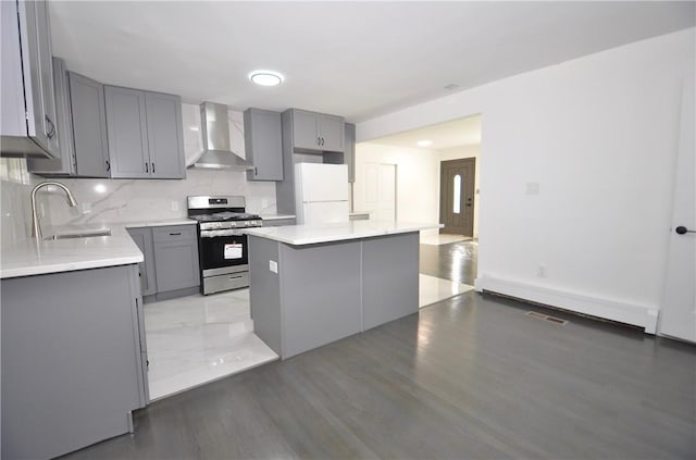 kitchen featuring a baseboard heating unit, wall chimney range hood, white refrigerator, a kitchen island, and stainless steel range with gas stovetop