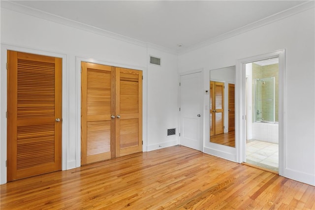 unfurnished bedroom featuring connected bathroom, light hardwood / wood-style flooring, multiple closets, and crown molding