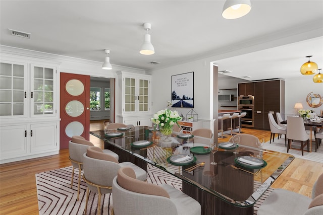dining area with ornamental molding, light wood-style flooring, and visible vents
