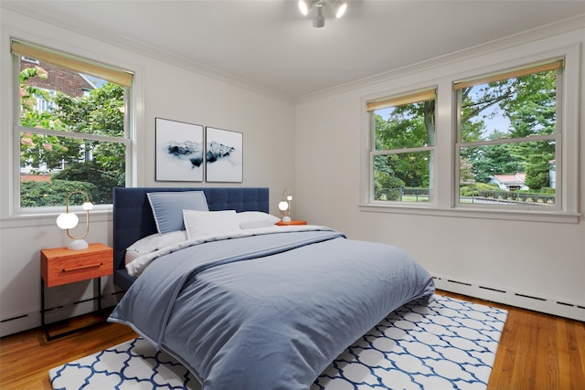 bedroom featuring crown molding, a baseboard heating unit, and wood finished floors
