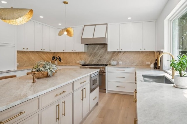 kitchen with premium range hood, light stone counters, white cabinets, decorative light fixtures, and sink