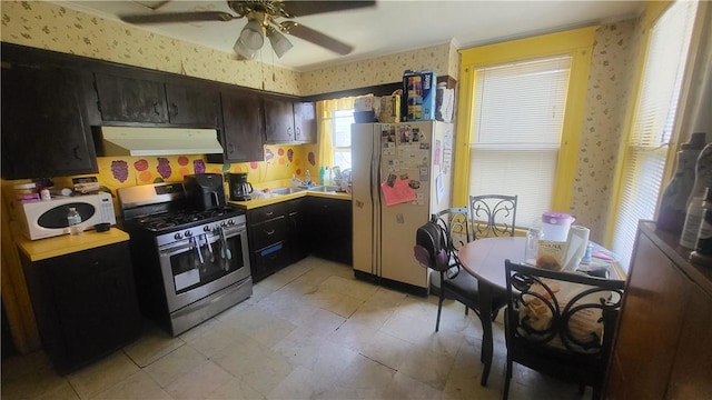 kitchen with wallpapered walls, ventilation hood, stainless steel appliances, light countertops, and ceiling fan