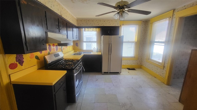 kitchen featuring wallpapered walls, under cabinet range hood, light countertops, freestanding refrigerator, and stainless steel gas range